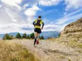 Biegacz w żółtej koszulce pokonuje kamienisty szlak. W tle góry i błękitne niebo z chmurami. To prawdziwe wyzwanie na rykowisko ultra trail.