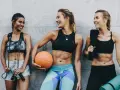 Trzy uśmiechnięte kobiety po treningu. Jedna trzyma skakankę, druga piłkę, trzecia ręcznik i matę. Widzą, co daje sport!