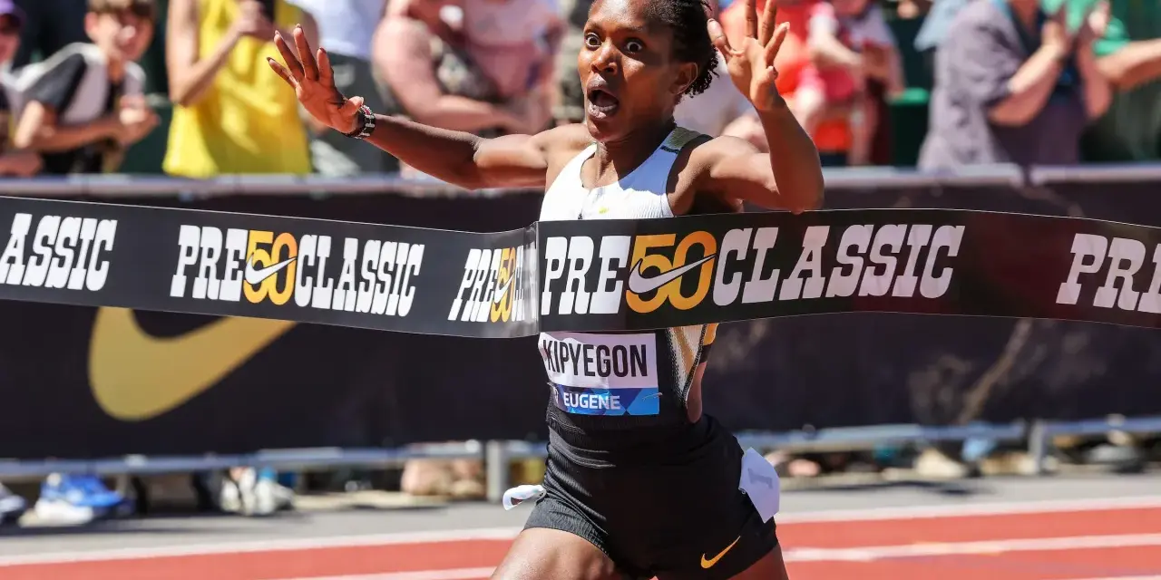 Faith Kipyegon przekracza linię mety z uniesionymi rękami, triumfując na bieżni.