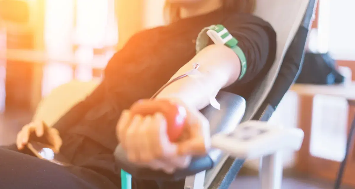 Uśmiechnięta osoba oddaje krew, ściskając czerwoną piłeczkę. Po oddaniu krwi warto pamiętać o nawodnieniu i lekkim posiłku.