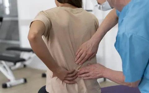 Fizjoterapeuta bada plecy pacjentki, która odczuwa ból po upadku na plecy. Konsekwencje urazu są widoczne.