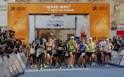 Zawodnicy przekraczają linię startu Maratonu Cracovia. Tłum kibiców z telefonami dokumentuje to wydarzenie.