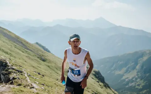 Zawodnik z numerem 111 biegnie pod górę podczas Tatra Sky Marathon. W tle piękne, mgliste pasmo górskie.