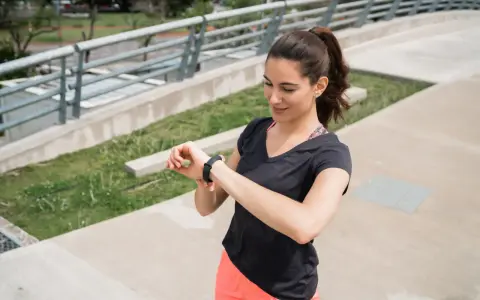 Kobieta w sportowym stroju sprawdza na zegarku tętno 180 po intensywnym treningu na zewnątrz.
