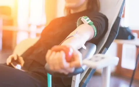 Uśmiechnięta osoba oddaje krew, ściskając czerwoną piłeczkę. Po oddaniu krwi warto pamiętać o nawodnieniu i lekkim posiłku.